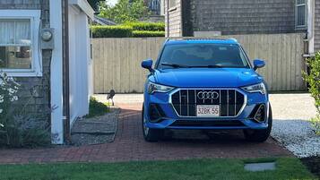 Ein blauer Audi steht auf einer Auffahrt mit einem Ziegelweg, der zu einem Haus führt.