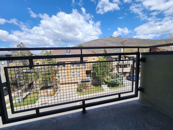 Un balcon doté d’une rambarde en métal, donnant sur un quartier résidentiel avec des maisons et des arbres.