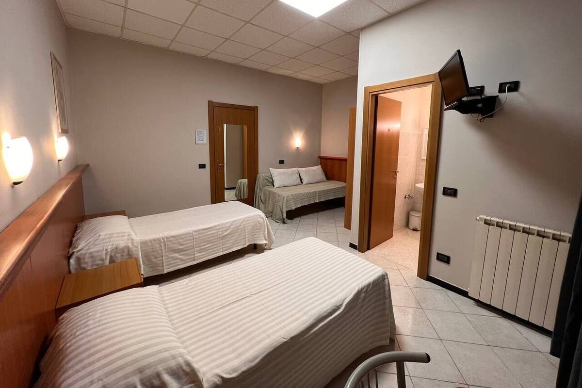 A hotel room with two beds, a wooden headboard, a wall-mounted TV, a radiator, and a bathroom visible through an open door.