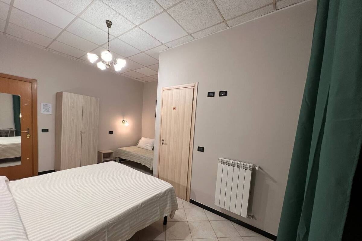 A hotel room with a bed, a wardrobe, a desk, and a radiator.