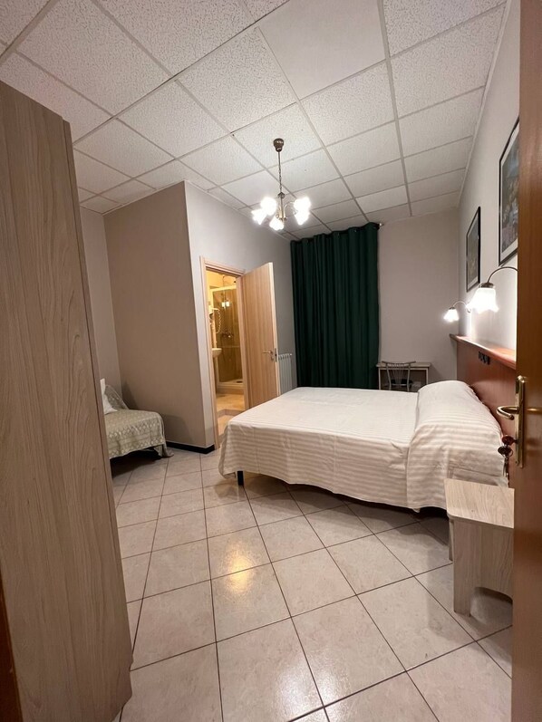 A bedroom with a bed, a desk, a chair, a door, and a shower area. - Shelter Affittacamere (Genoa)