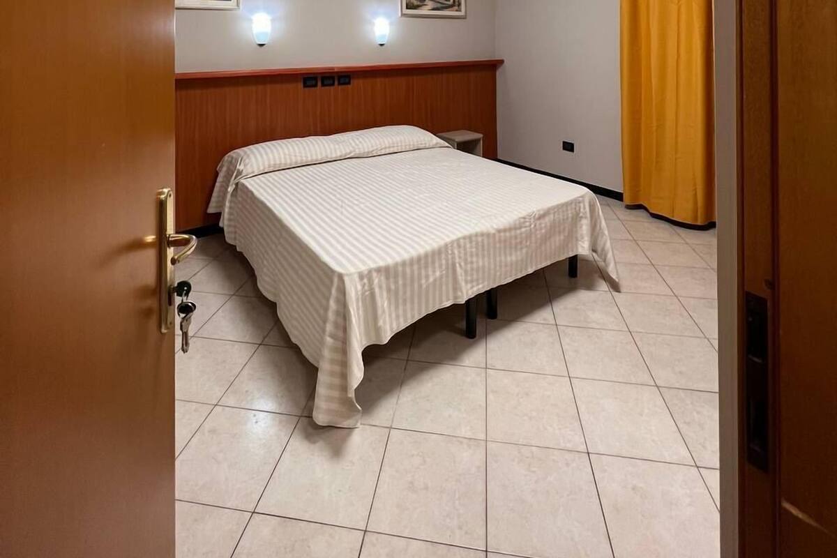 A hotel room with a bed, a wooden headboard, a small table, and a yellow curtain.