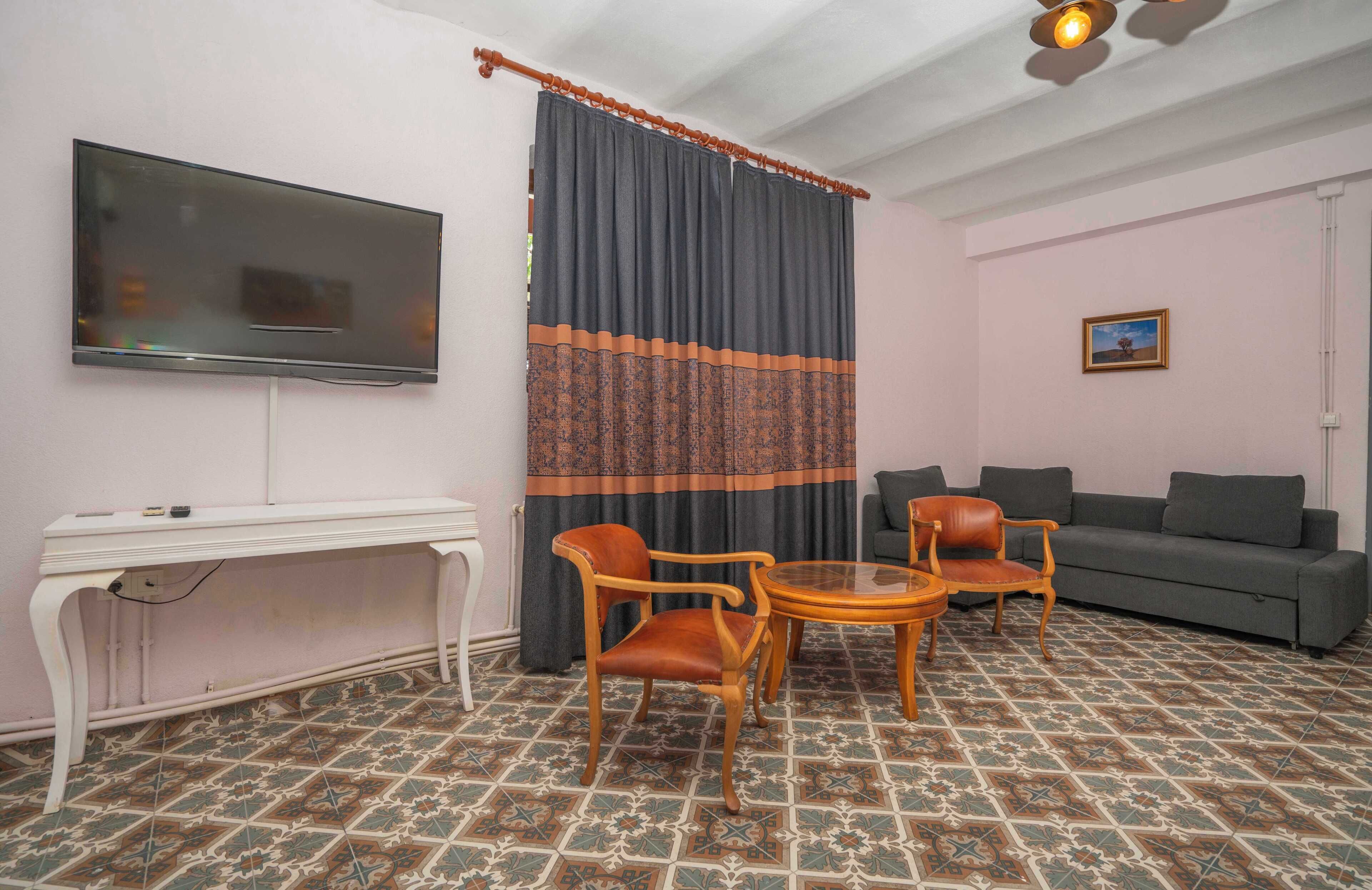 Una sala de estar con televisor, sofá, dos sillones, una mesita y baldosas de suelo estampadas.