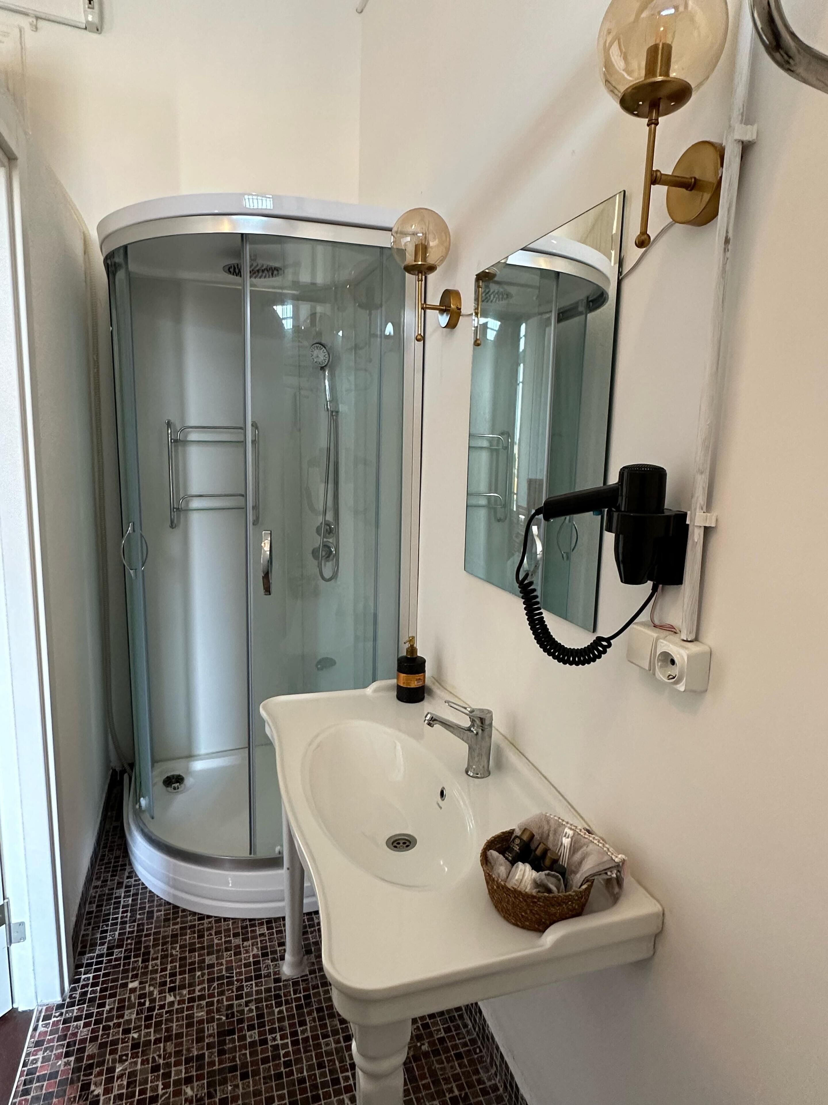 A bathroom with a glass-enclosed shower, a white sink, and a mirror with a wall-mounted telephone.