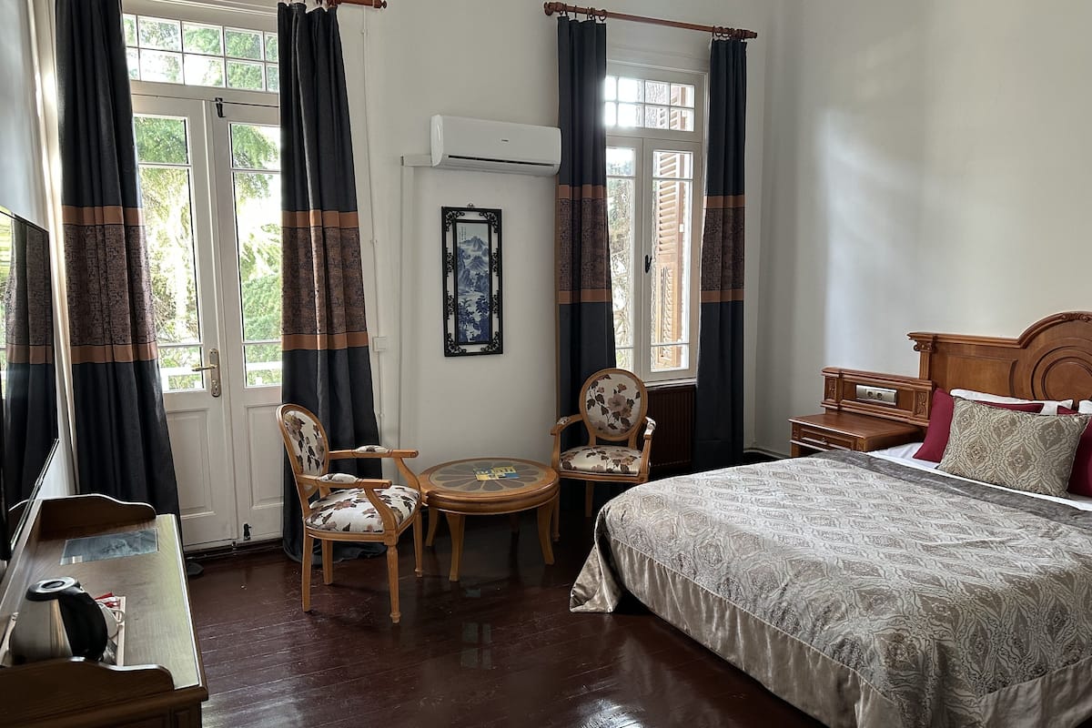 A bedroom with a bed, a chair, a small table, and a window with curtains.