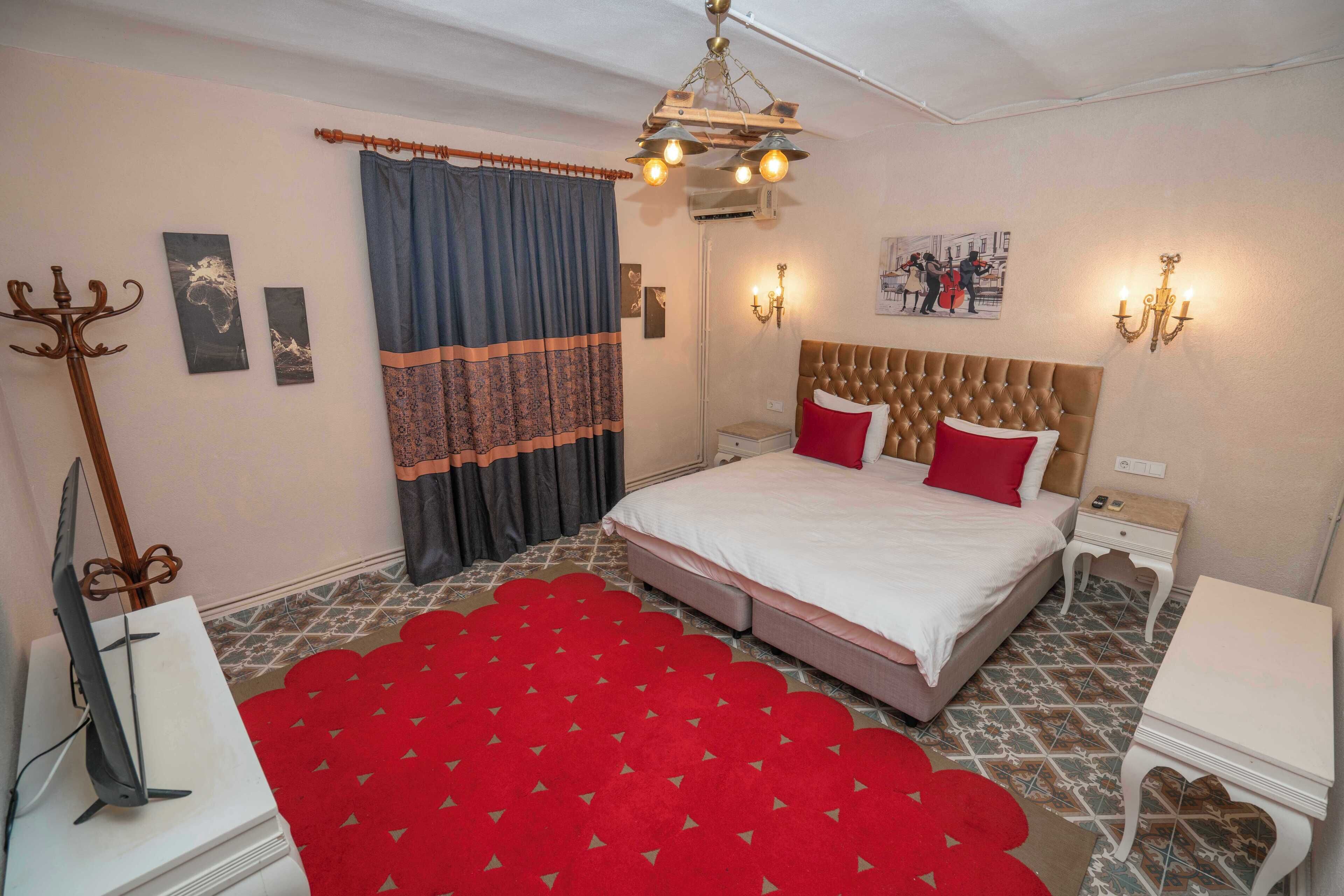 A bedroom with a large bed, a red carpet, a chandelier, and a wall-mounted artwork.
