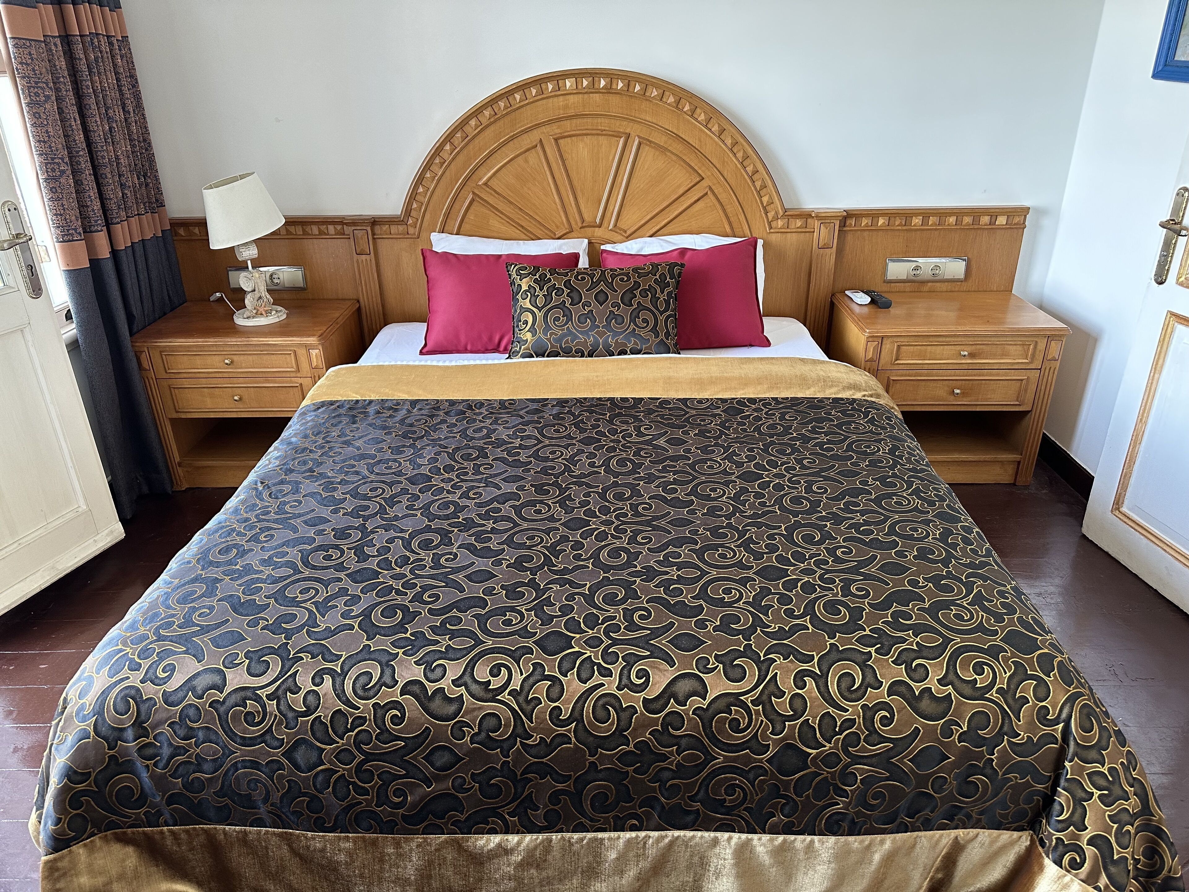 A hotel room with a large bed, wooden headboard, two bedside tables with lamps, and a nightstand with a phone.
