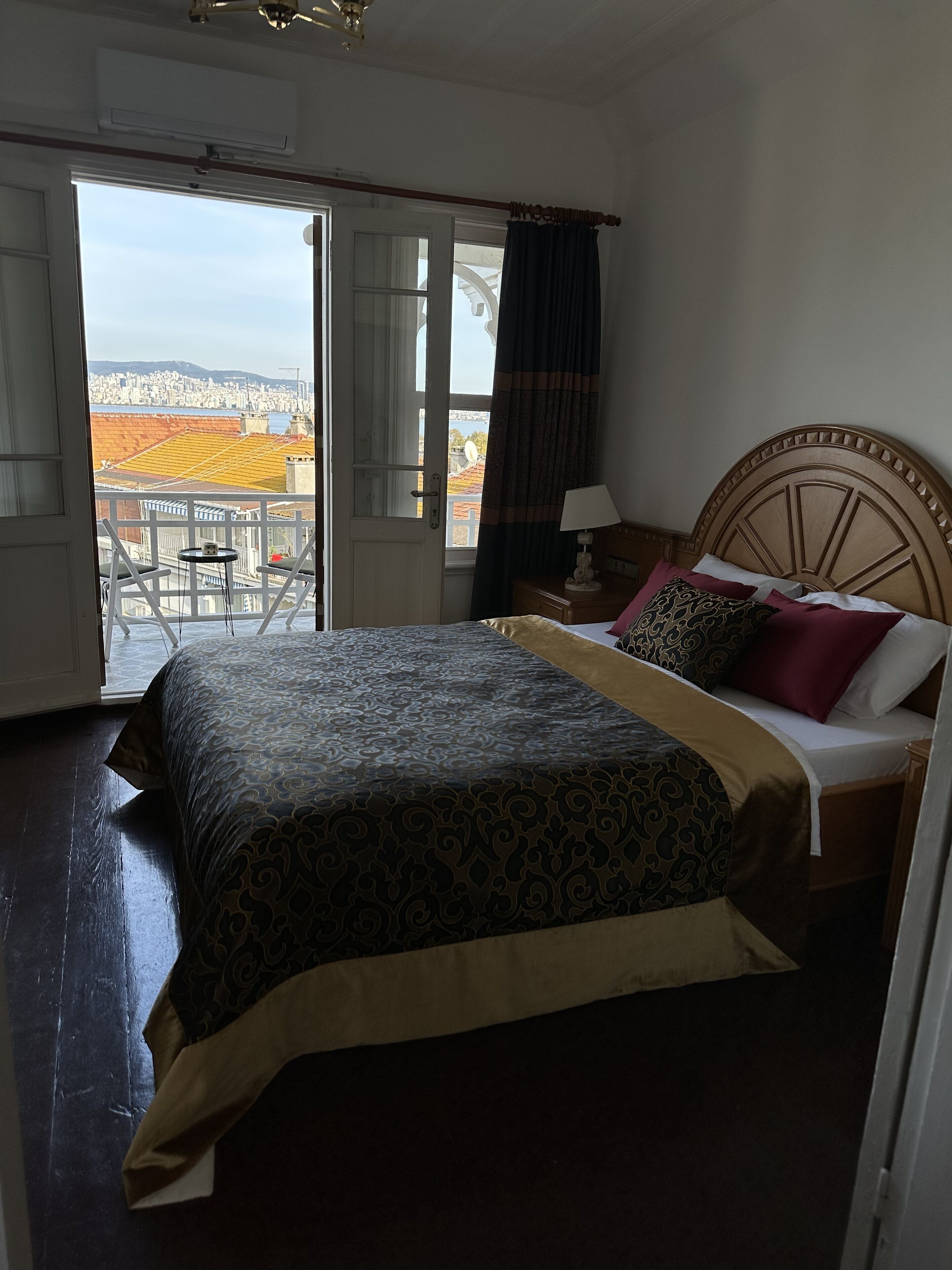Un dormitorio con cama, una mesita de noche, una lámpara y vistas de la ciudad a través de una puerta abierta.