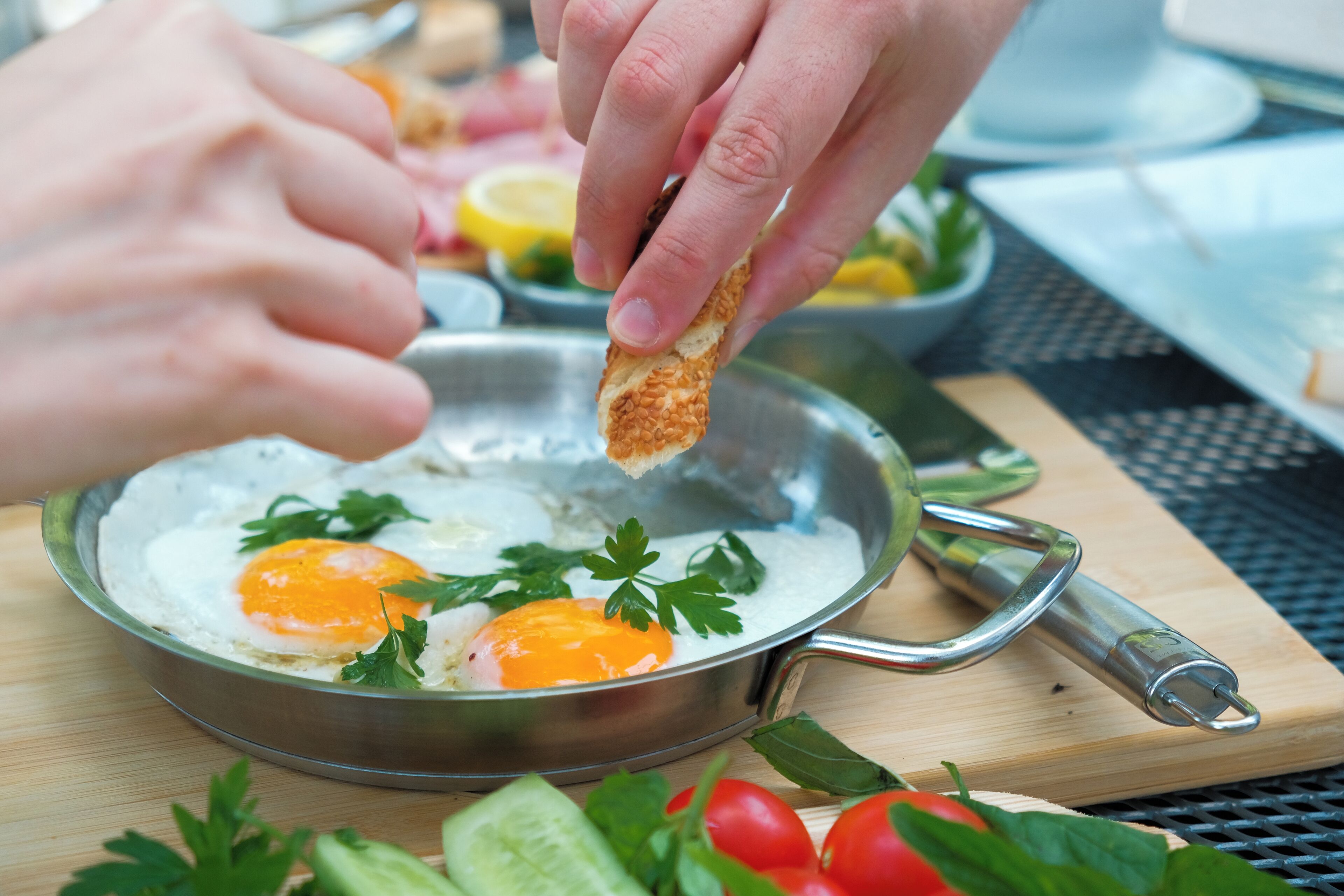 A person holding a piece of bread over a pan with eggs and parsley.