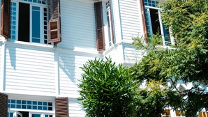 A two-story building with white exterior walls, brown shutters, and a balcony with ornate railings. - Laden Palas Hotel Buyukada (Adalar)
