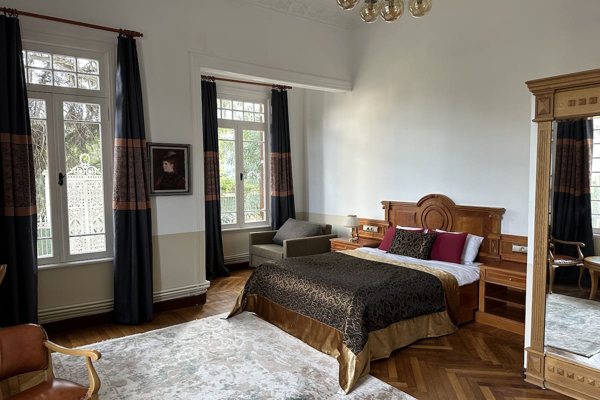 A bedroom with a large bed, a wooden headboard, a chair, a nightstand, and a mirror.