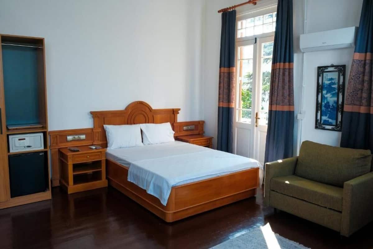 A bedroom with a wooden bed, bedside tables, a chair, a wardrobe, and a window with curtains.