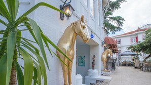 A courtyard with a golden horse statue, a palm tree, and a white building with red shutters. - Laden Palas Hotel Buyukada (Adalar)