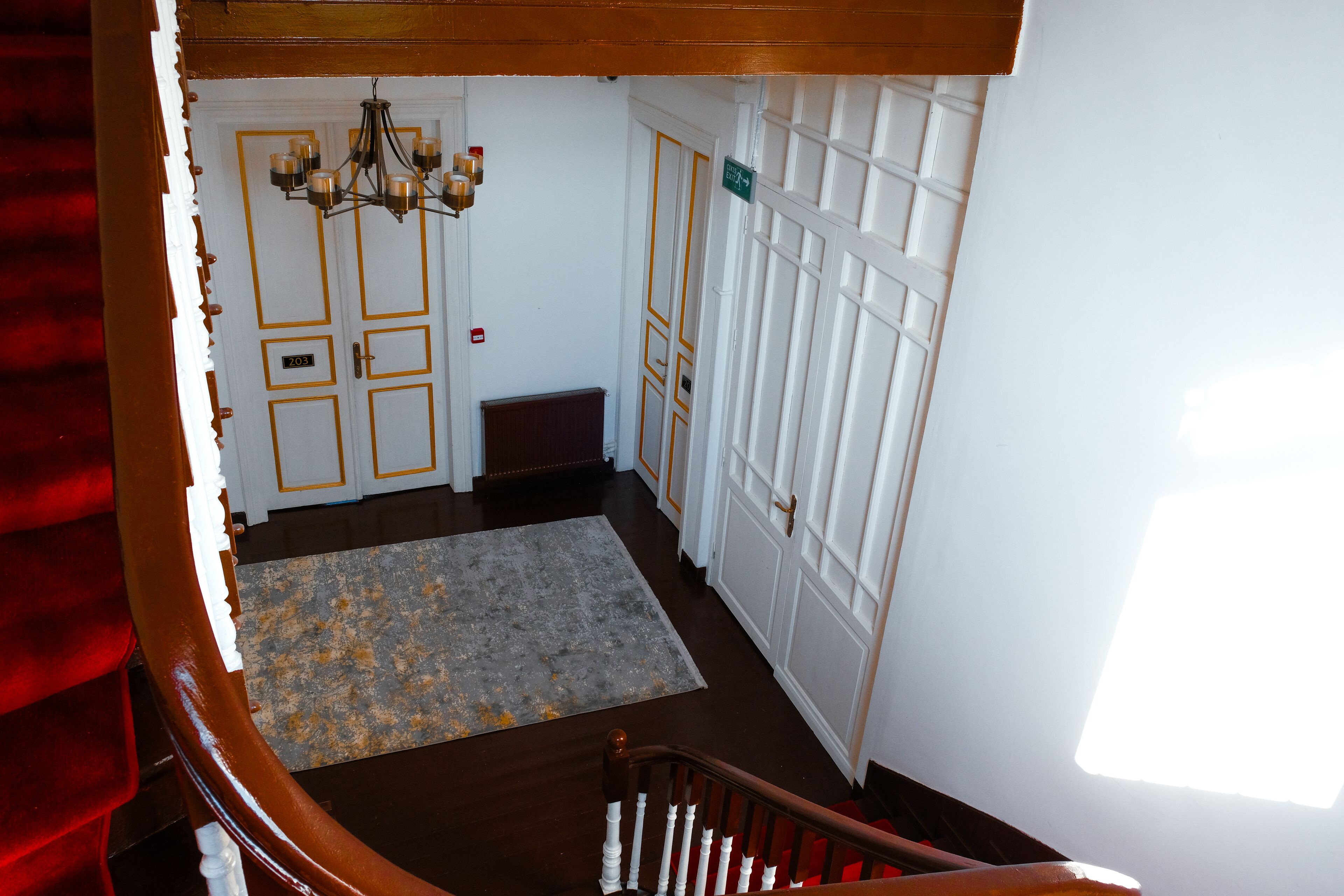 Un escalier menant à une pièce où se trouve un lustre, une porte portant un numéro et une fenêtre.
