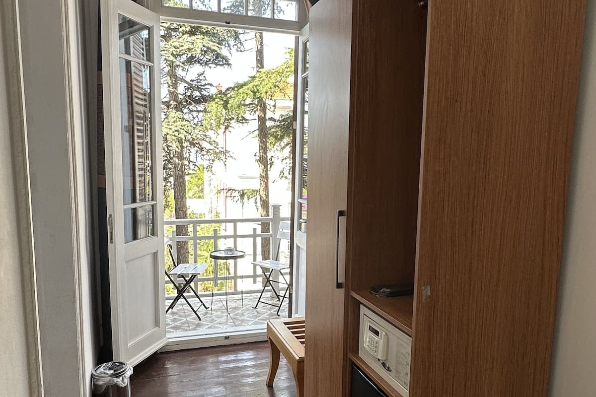 A room with a wooden wardrobe, a small table, and a bench outside a door leading to a balcony.