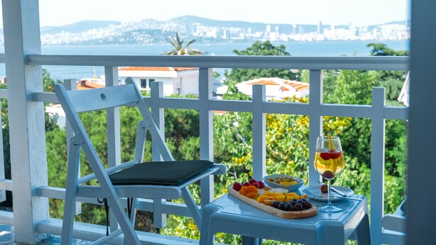 A balcony with a table set for a meal, a glass of drink, and a view of a cityscape. - Laden Palas Hotel Buyukada (Adalar)