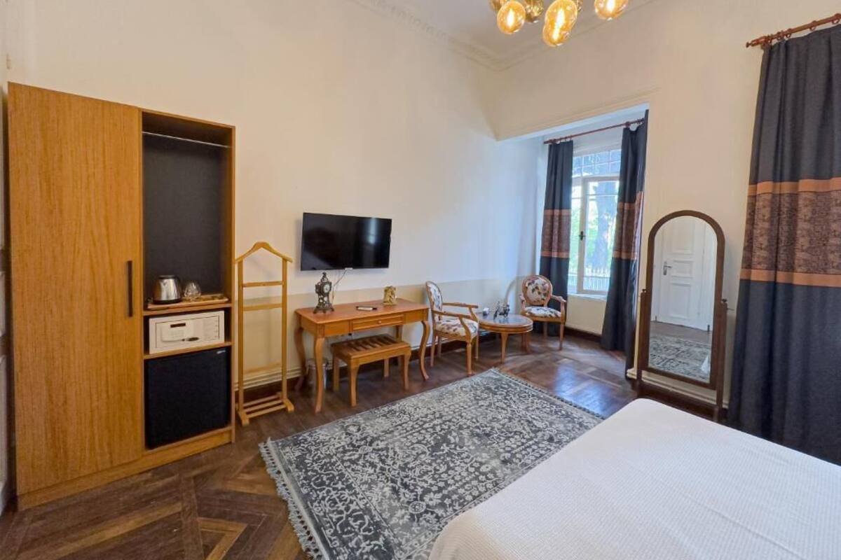A bedroom with a bed, a desk, a chair, a television, a wardrobe, and a mirror.
