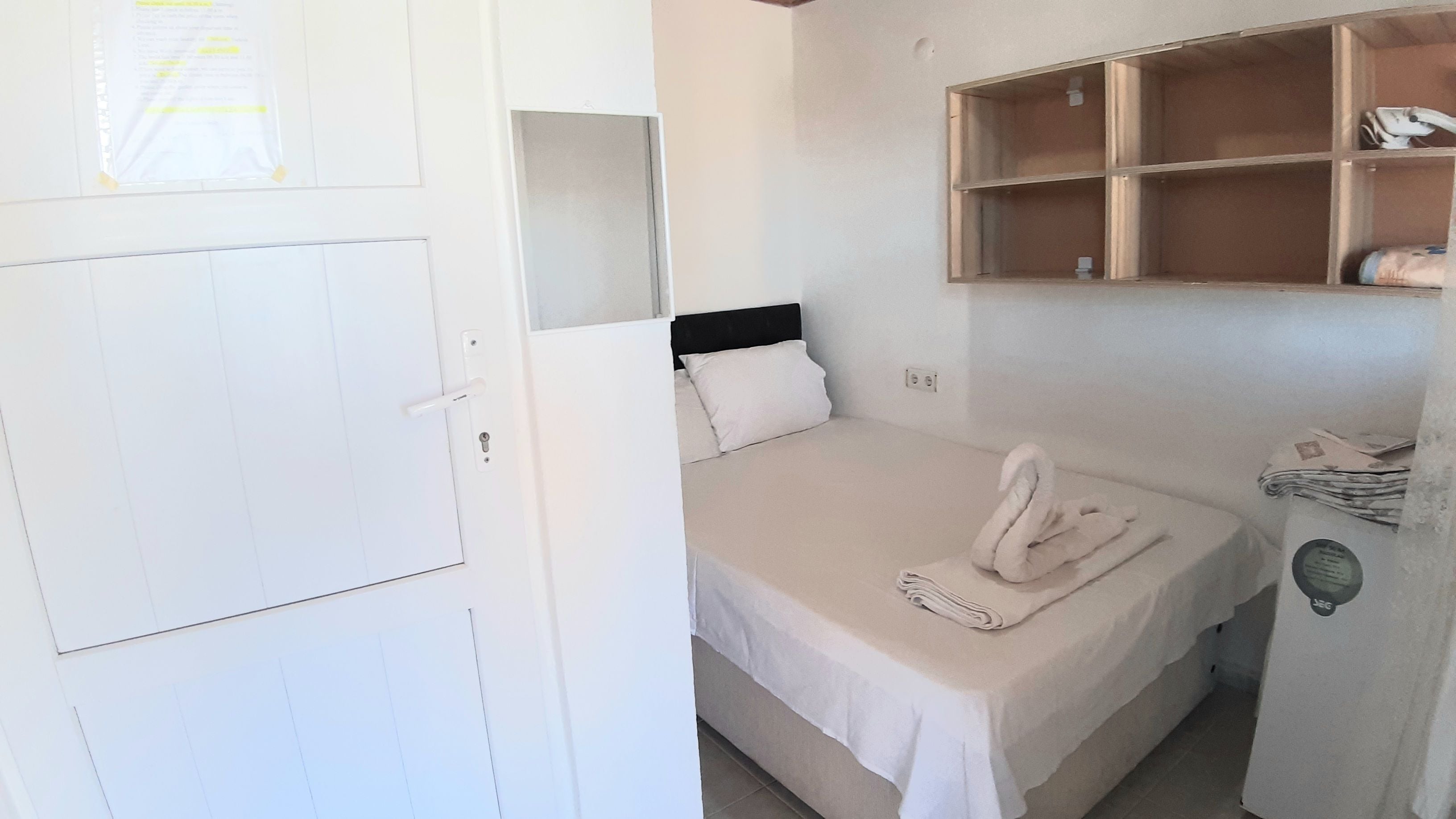 Una cama individual con cabecera, una puerta blanca y un estante con objetos.