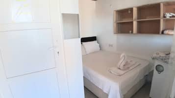 Una cama individual con cabecera, una puerta blanca y un estante con objetos.