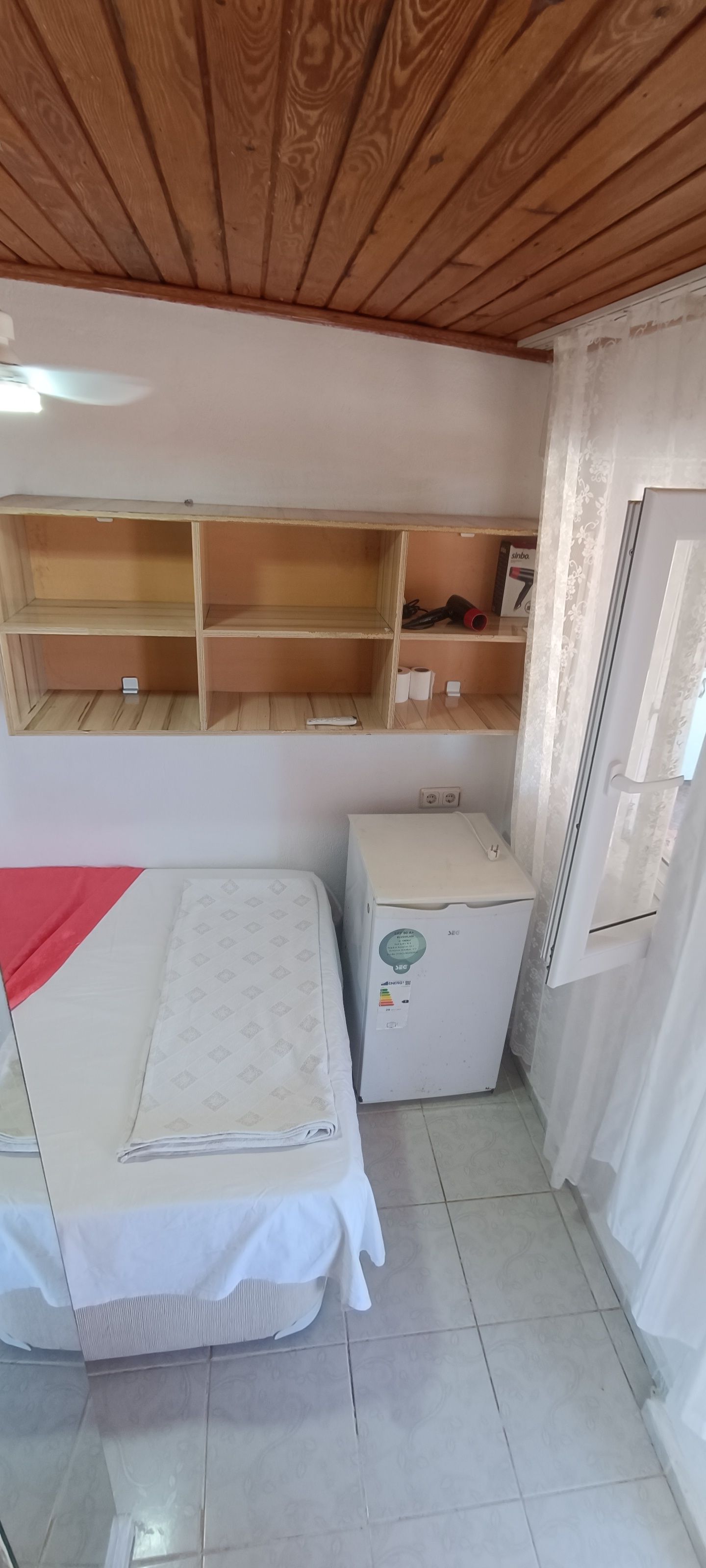 Una habitación pequeña con cama, refrigerador y estantería.
