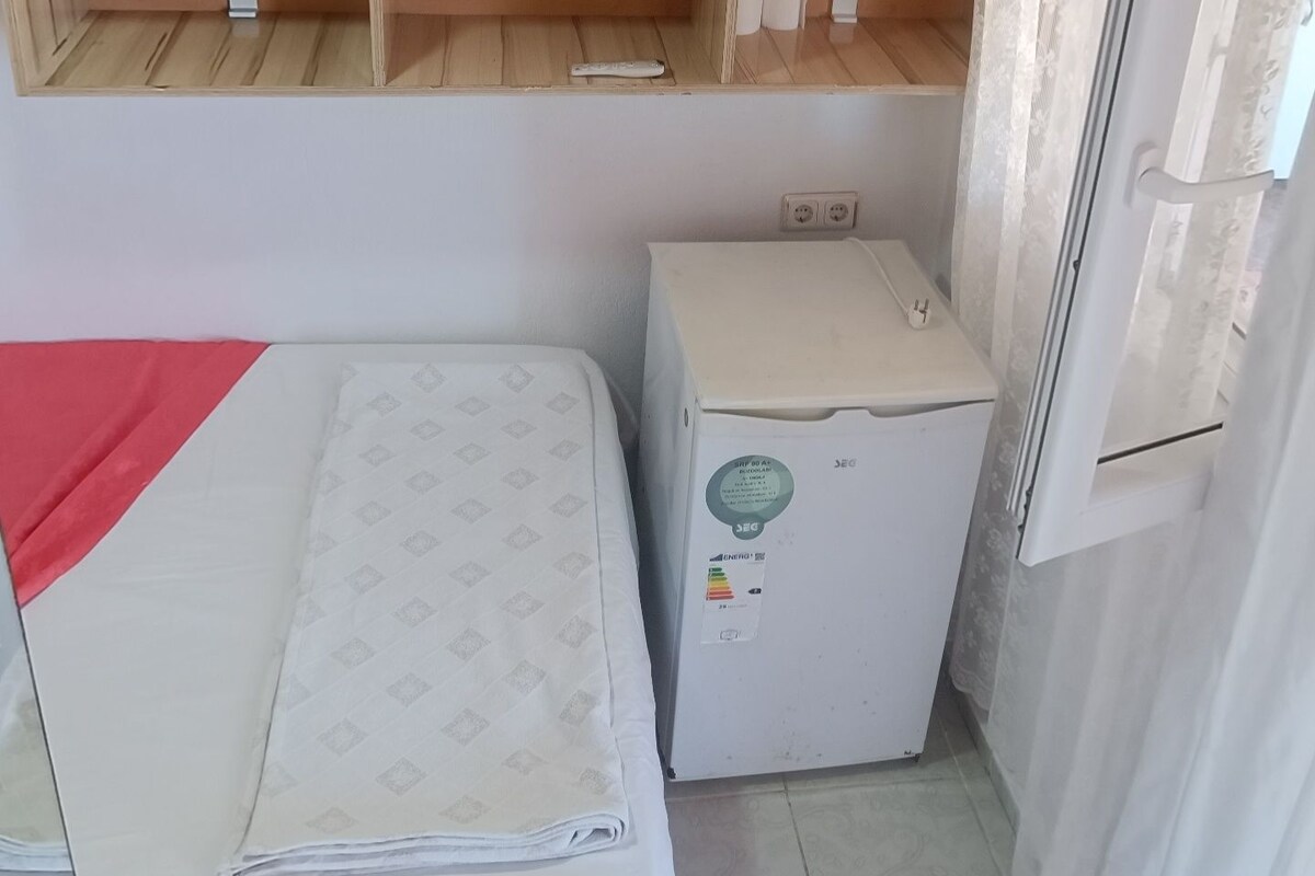 Une petite pièce comprenant un lit, un réfrigérateur et une étagère.
