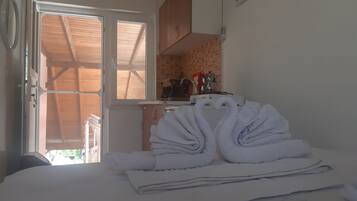 A room with a bed, a window with a view of a wooden structure outside, and a kitchenette with a stove and sink.