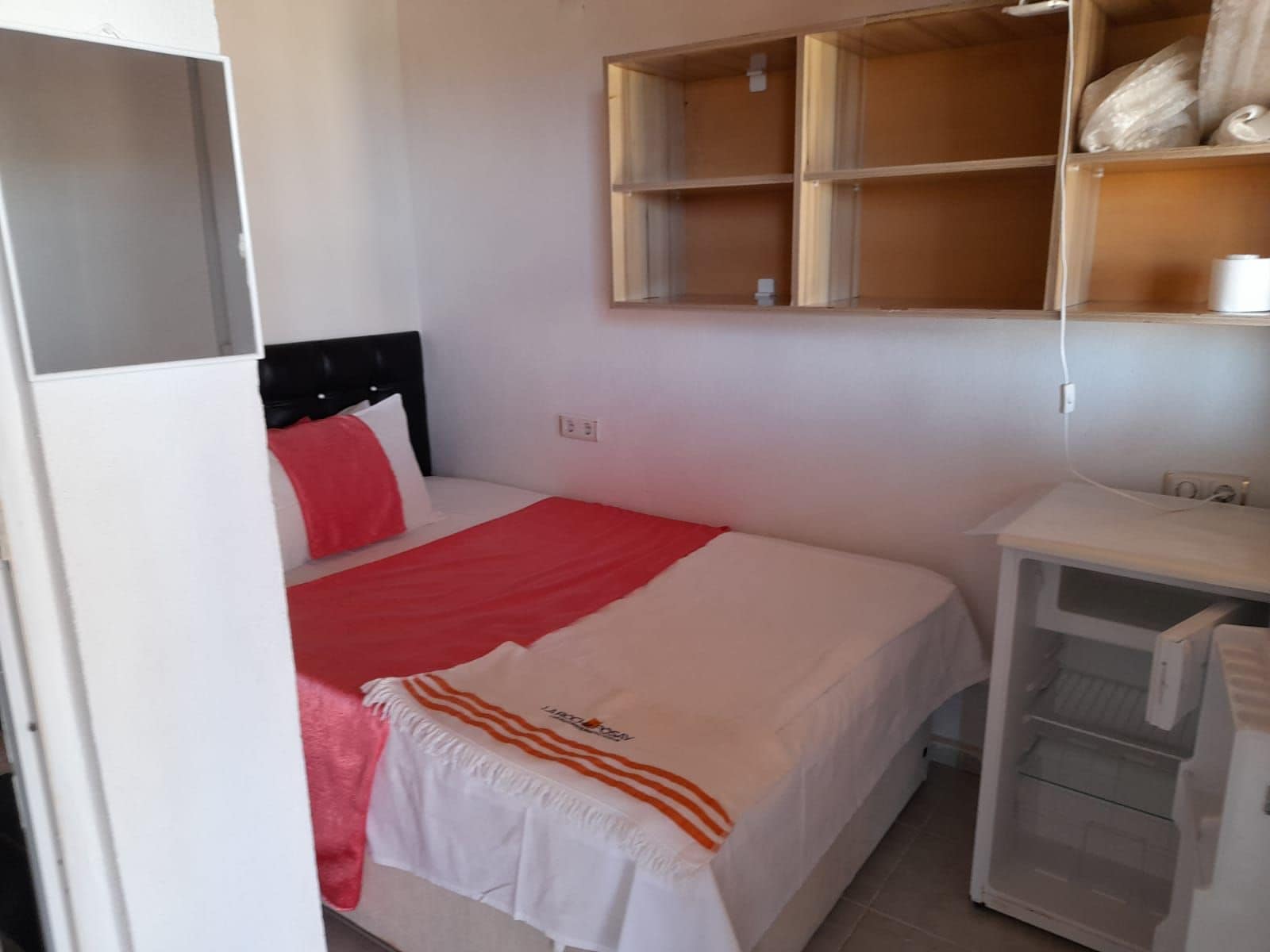 A bedroom with a bed, a bedside table, a mirror, and a built-in wardrobe.