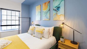 A modern bedroom with a bed, bedside table, lamp, and abstract wall art. - At the level - (2 bed flat) (Brighton and Hove)