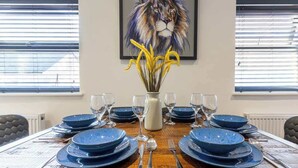 A dining table set for six with blue plates and silverware, a vase with yellow flowers, and a framed painting of a lion on the wall. - At the level - (2 bed flat) (Brighton and Hove)