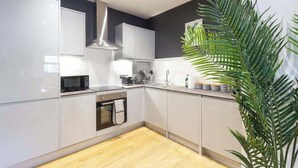 A modern kitchen with white cabinets, a stainless steel range hood, and a wooden floor. - At the level - (2 bed flat) (Brighton and Hove)