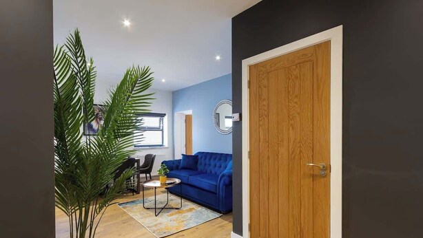 A living room with a blue sofa, a wooden door, and a potted plant. - At the level - (2 bed flat) (Brighton and Hove)