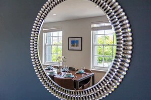 A dining area with a round mirror, a table set with plates, glasses, and a vase of flowers. - Albion at the Level - 2 BD Flat (Brighton and Hove)