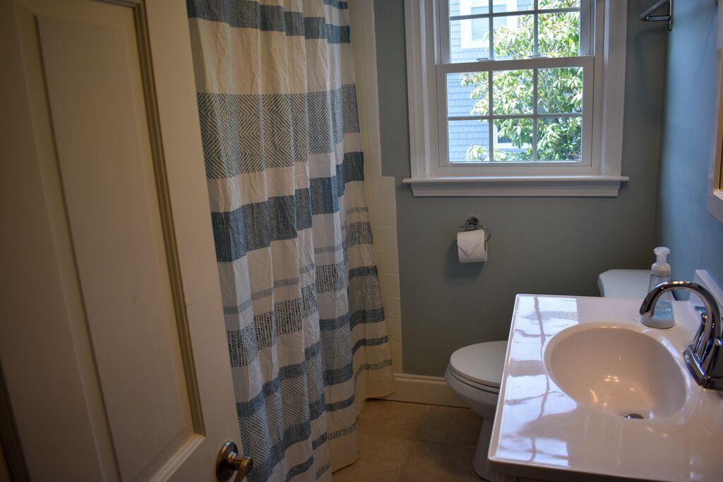 Un baño con lavamanos blanco, inodoro y ventana con vistas a árboles.