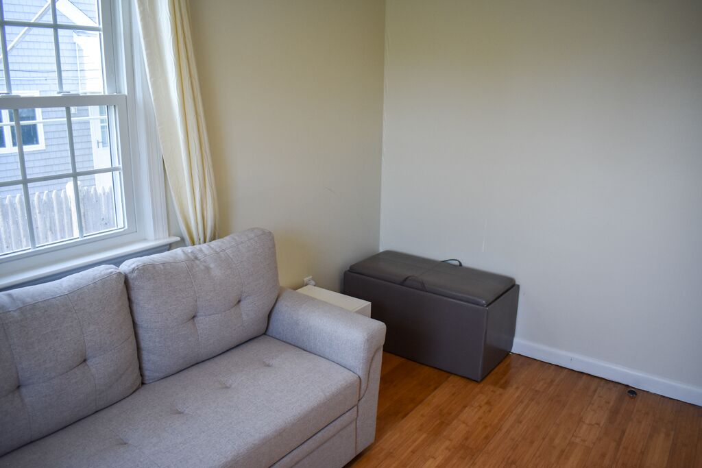 A living room with a grey sofa, a small grey ottoman, and a white radiator.