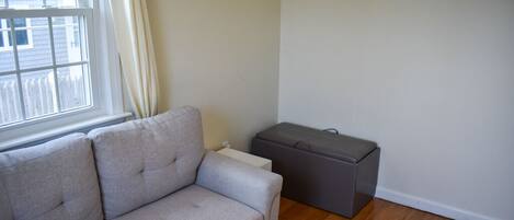 A living room with a grey sofa, a small grey ottoman, and a white radiator.
