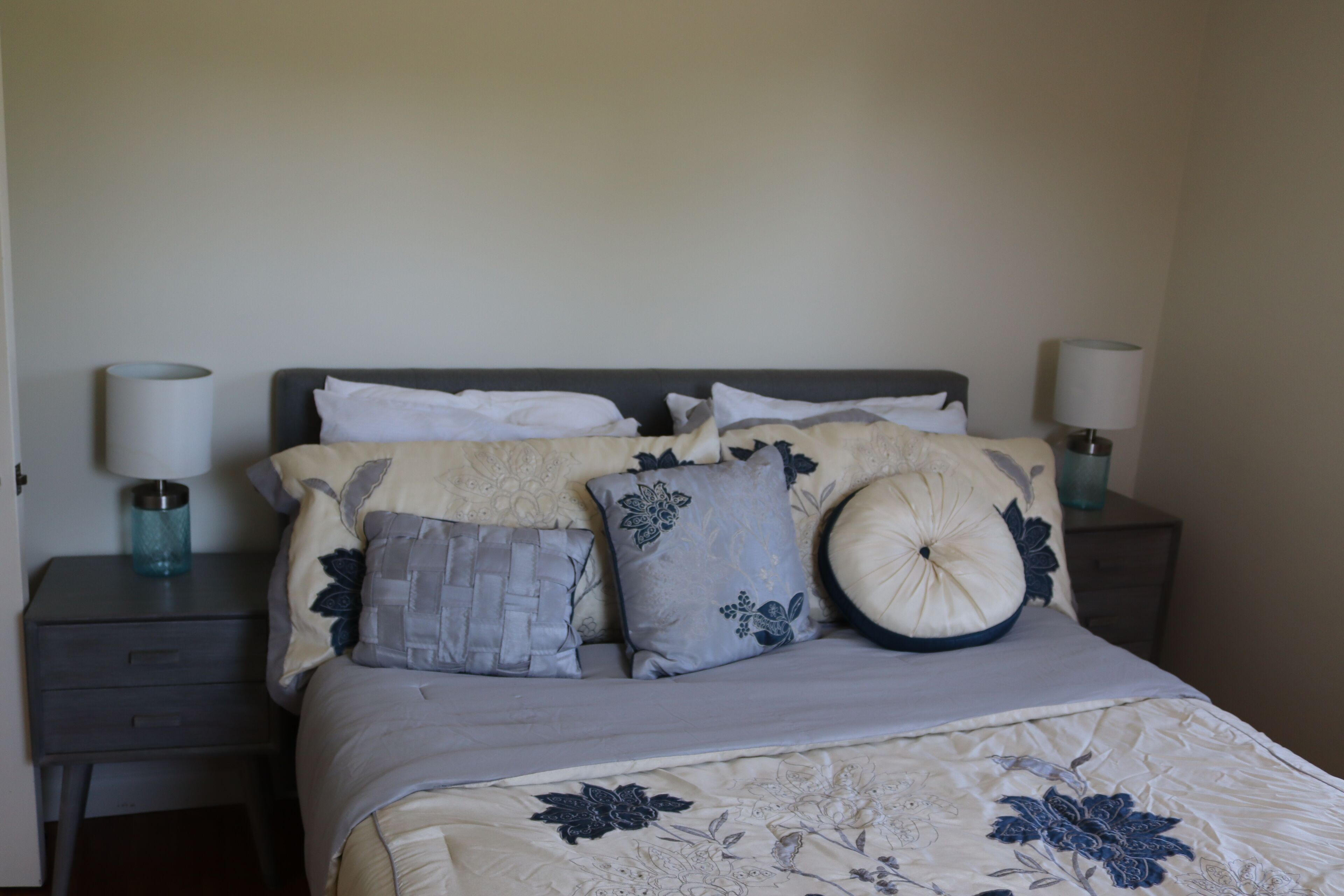 A neatly made bed with a floral-patterned bedspread, two bedside tables with lamps, and a wall with a subtle textured pattern.