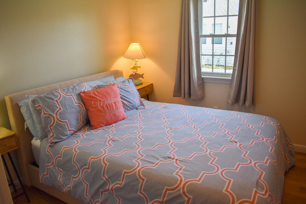 A bedroom with a bed, a nightstand, a lamp, and a window with curtains.