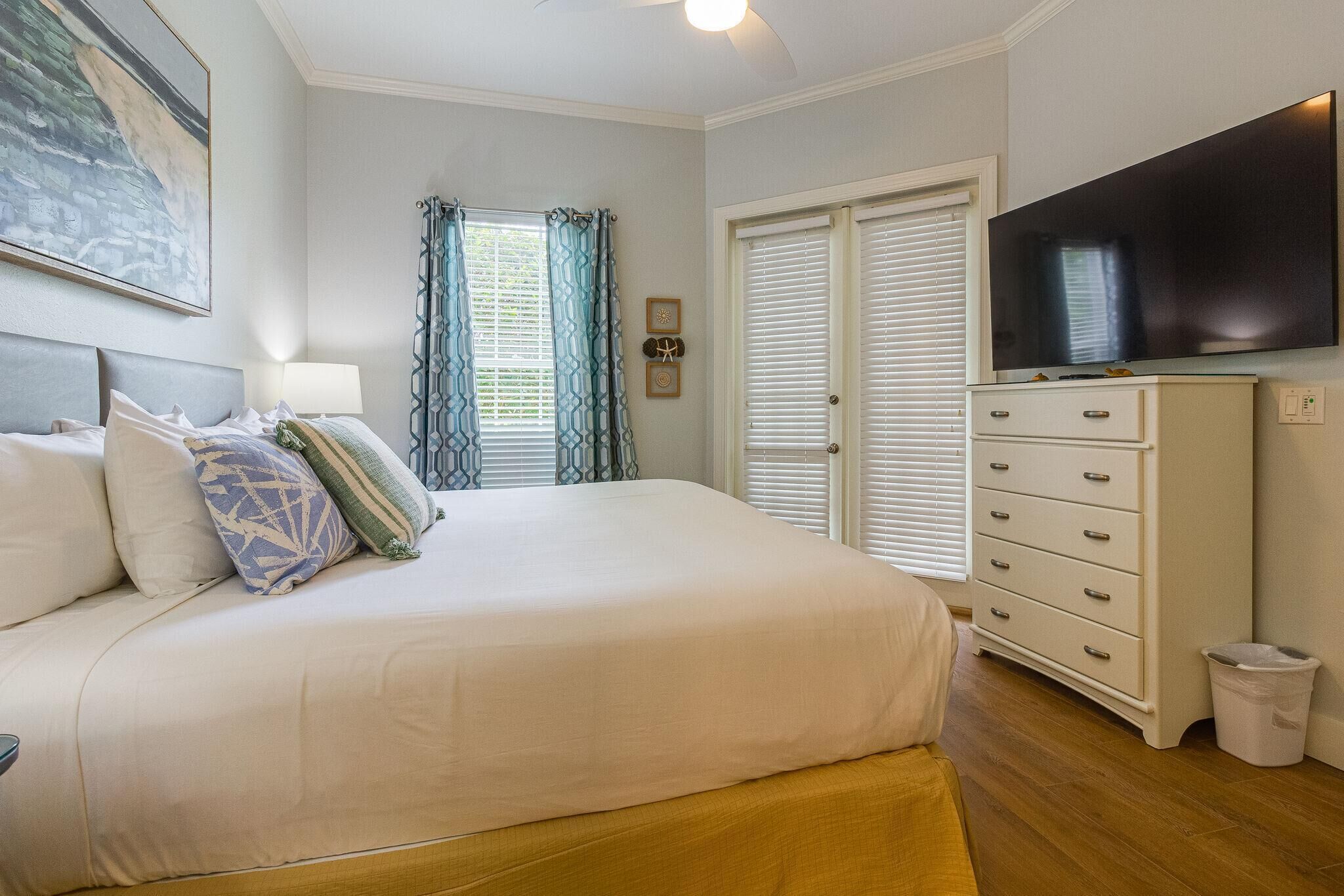 A bedroom with a large bed, a television, a dresser, and a window with curtains.