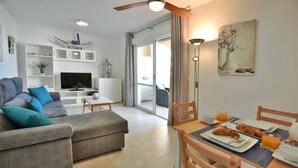 Una sala de estar moderna con un sofá gris, una mesa de comedor con alimentos para el desayuno y un televisor sobre un mueble blanco.