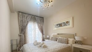 A bedroom with a large bed, a bedside table with a lamp, and a ceiling light fixture. - Alq 048 Porto Azul 2 (Calpe / Calp)
