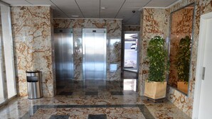 A marble-floored lobby with two elevators, a trash bin, and potted plants. - Alq 048 Porto Azul 2 (Calpe / Calp)