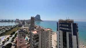 Eine Küstenstadt mit Hochhäusern, einem Strand und einer markanten Felsformation in der Ferne.