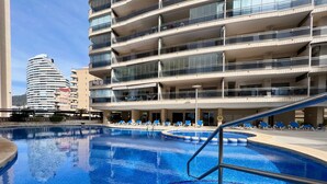 Ein Pool mit blauen Fliesen, umgeben von Liegestühlen und einem mehrstöckigen Gebäude mit Balkonen.