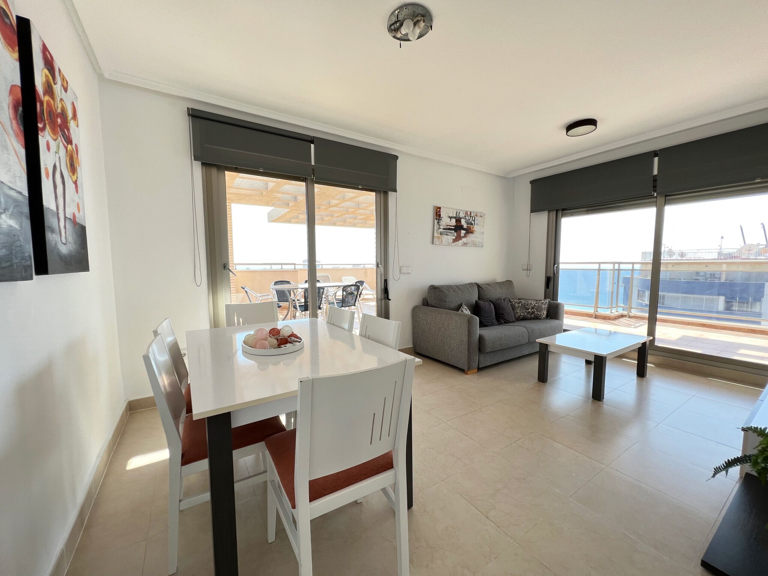 A modern living room with a dining area, large windows, and a balcony with a view.