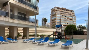 Eine Dachterrasse mit blauen Liegestühlen und einer Spielanlage für Kinder.