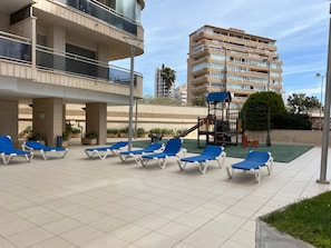 A rooftop lounge area with blue lounge chairs and a children's play structure. - Alq 066 Atico Bahia del Sol (Calpe / Calp)