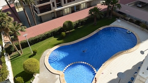 An aerial view of a swimming pool surrounded by a landscaped area with palm trees and a red-roofed building in the background. - Alq 128 Bahia del Sol (Calpe / Calp)