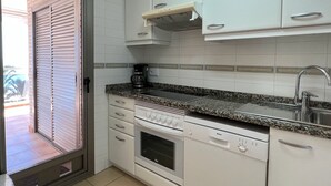 A compact kitchen with white cabinets, a built-in oven, a dishwasher, and a granite countertop. - Alq 128 Bahia del Sol (Calpe / Calp)