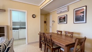 A dining area with a wooden table and chairs, a kitchen visible through an open door, and two framed pictures on the wall. - Alq 128 Bahia del Sol (Calpe / Calp)