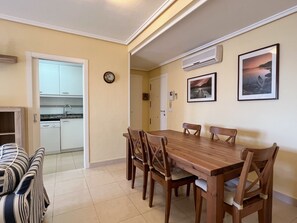 A dining area with a wooden table and chairs, a kitchen visible through an open door, and two framed pictures on the wall. - Alq 128 Bahia del Sol (Calpe / Calp)